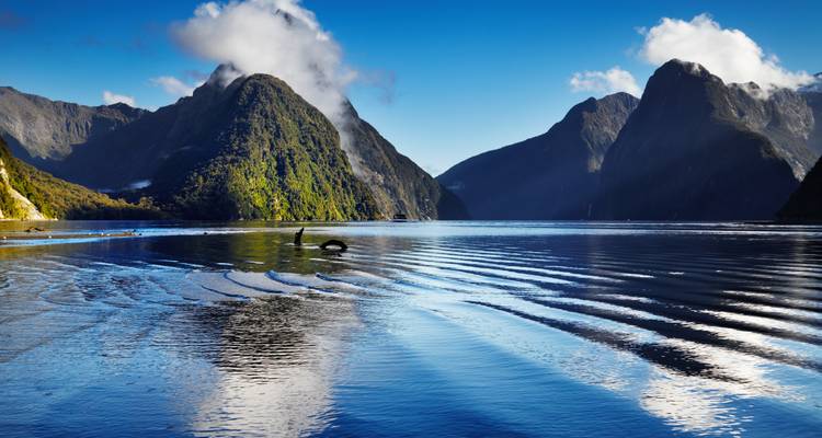 Scène dramatique de fjord avec d'imposantes falaises sombres et un pic distinctif en forme de pyramide se reflétant dans l'eau bleue immobile