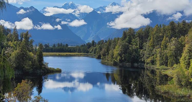 Lago que refleja montañas cubiertas de nieve, con bosques frondosos enmarcando la vista.