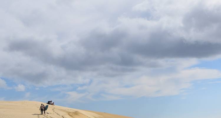 Eine weite Sanddüne mit Menschen, die darauf gehen, unter einem bewölkten Himmel.