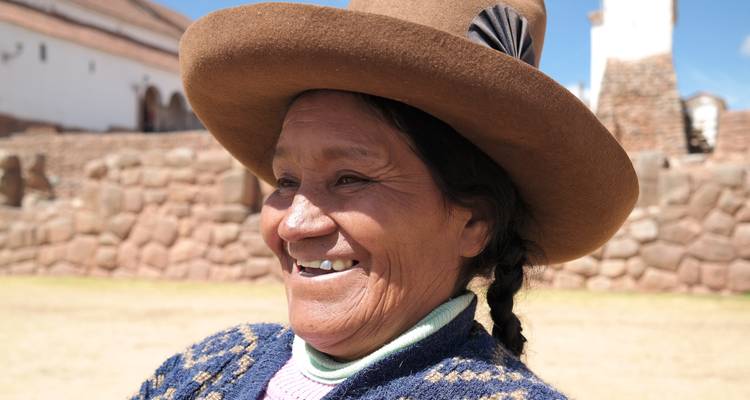 Une femme locale souriante en tenue traditionnelle avec un bâtiment historique en arrière-plan.