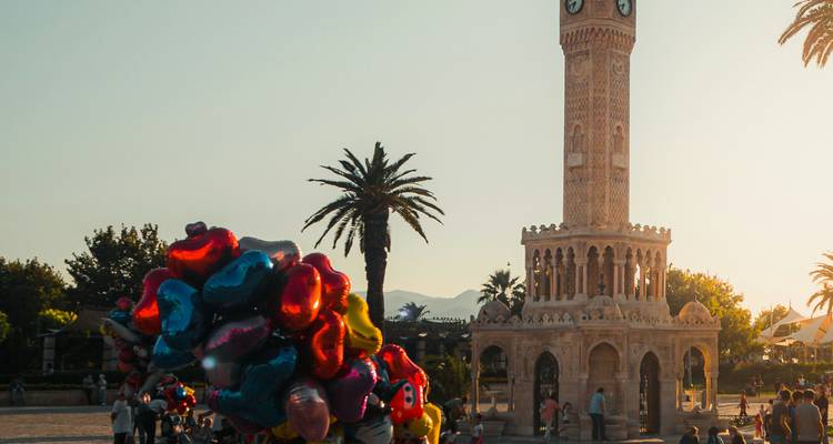 Tour d'horloge sur une place de ville avec des ballons et des palmiers.