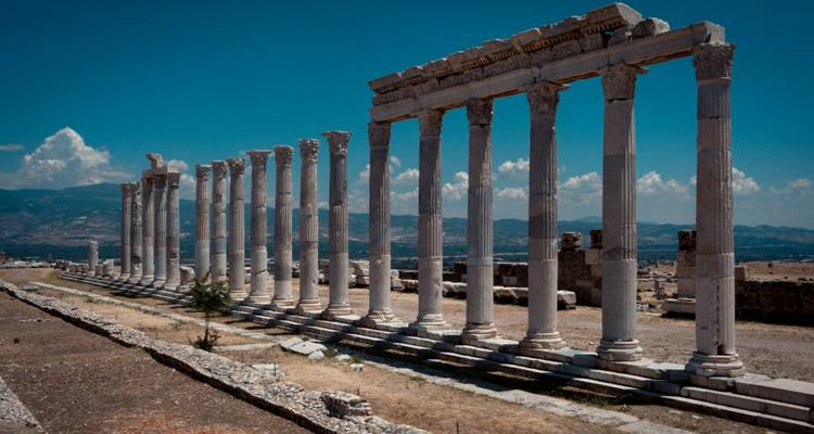 Longue rangée de colonnes antiques avec des montagnes en arrière-plan.