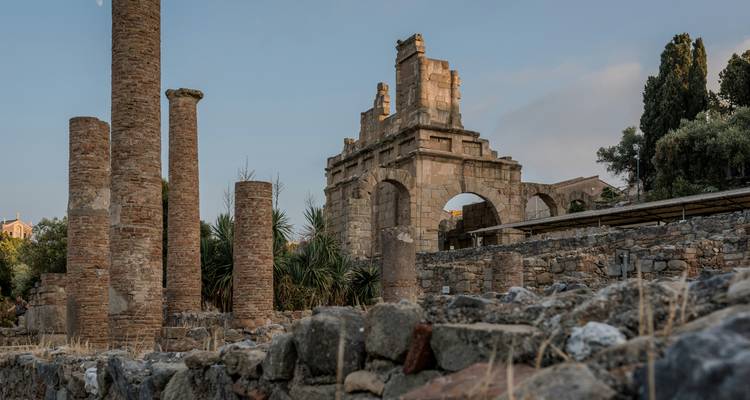 Ruines avec des arcs et des colonnes debout parmi d'autres structures anciennes.