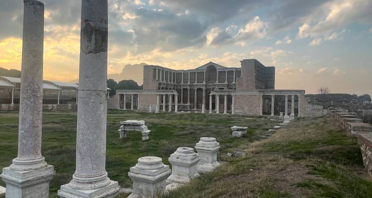 Ruines d'un bâtiment en pierre romain avec une zone herbeuse sous un ciel nuageux.