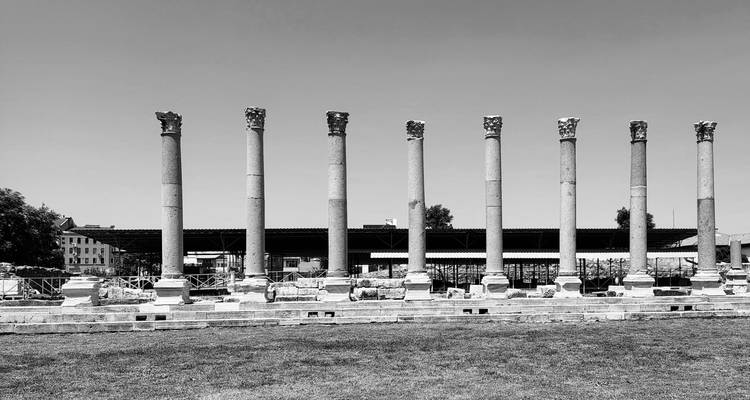 Image en noir et blanc de colonnes antiques avec des bâtiments de la ville derrière.