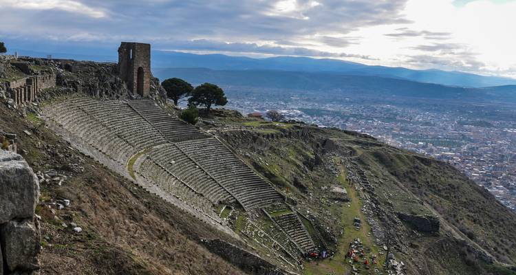 Ruines d'un amphithéâtre surplombant un paysage urbain moderne.