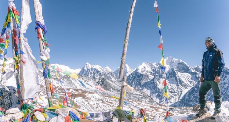 Une personne debout à côté de drapeaux de prière dans un paysage de montagne enneigé.