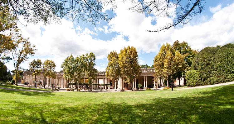 Large jardin avec des arbres et un bâtiment néoclassique.