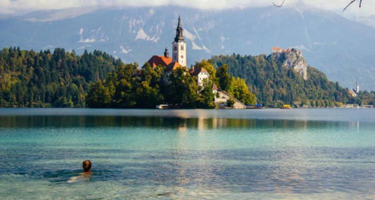 Una persona nadando en un lago con una iglesia en una isla y montañas.