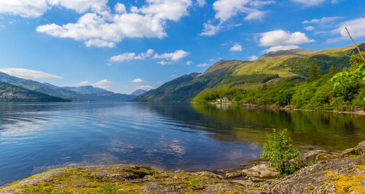 Ein malerischer Blick auf einen See mit Bergen und Bäumen unter einem blauen Himmel.