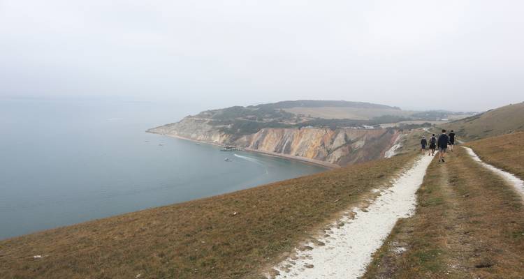 People walking on a coastal path with cliffs in the distance.
