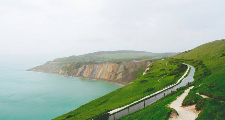 A road alongside steep cliffs and the sea under an overcast sky.