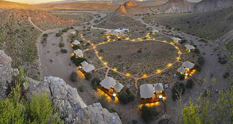 Vue aérienne d'un arrangement de lodges circulaire dans un paysage semi-désertique avec un éclairage doux.
