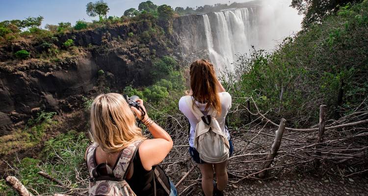 Deux personnes photographiant une grande cascade, entourées d'un feuillage luxuriant.