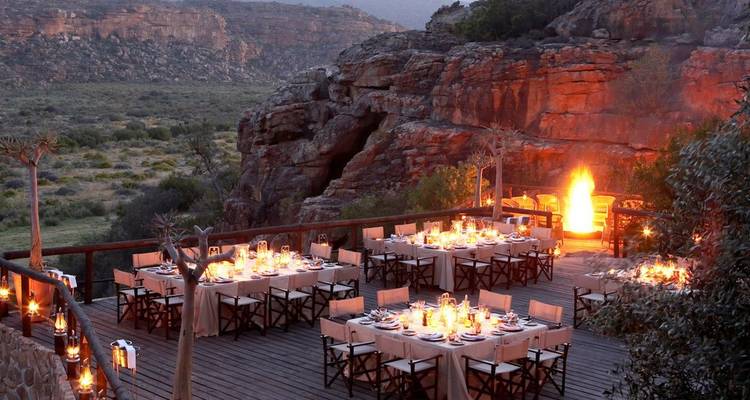 Espace de restauration en plein air aménagé avec des tables et des chaises, donnant sur un paysage rocheux sous la lumière du soir.