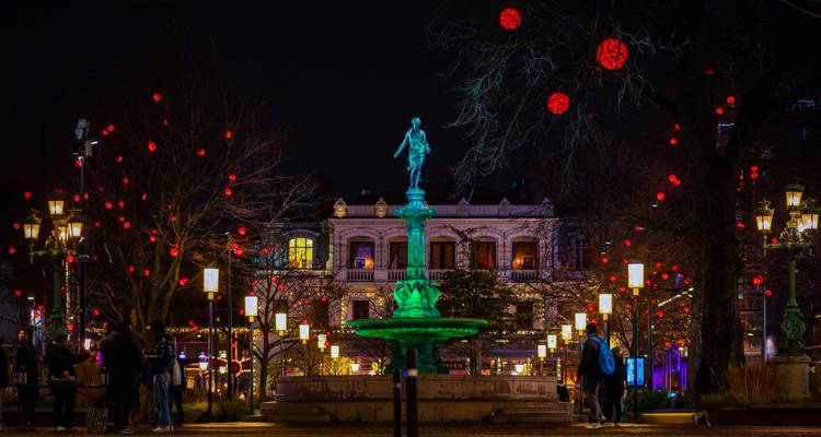 Fontaine vibrante et arbres décorés sur une place de ville pendant la nuit.