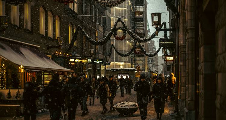Rue de ville enneigée animée avec des gens et décorée de lumières de fête.