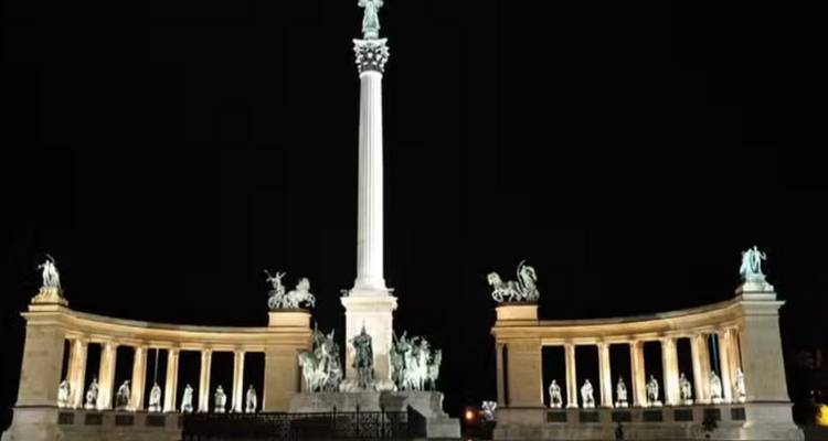 Un monument avec des colonnes à statues éclairé la nuit.
