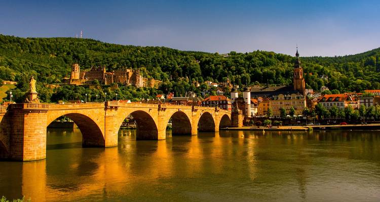 Pont historique enjambant une rivière avec une petite ville en arrière-plan.