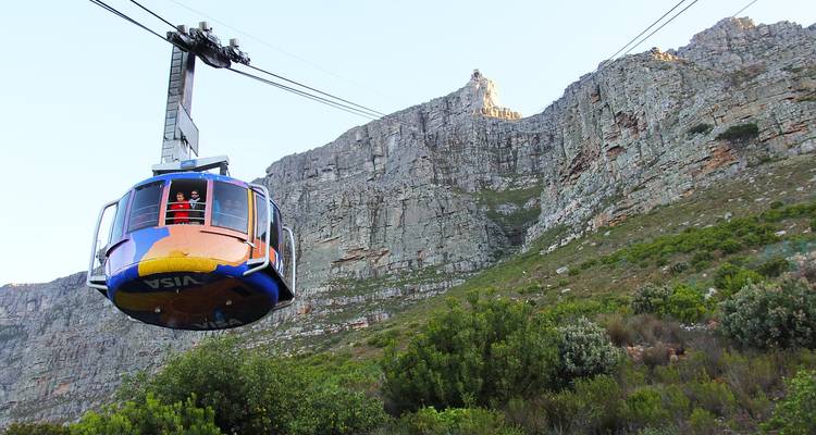 Teleférico contra una pared rocosa de montaña rodeada de vegetación.