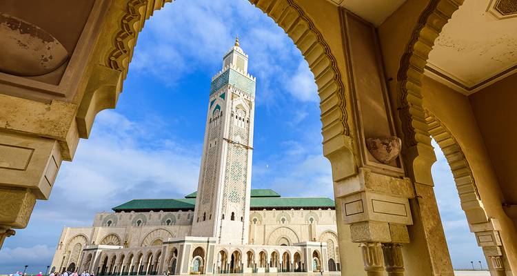 Une mosquée ornée vue à travers une arcade sous un ciel dégagé.
