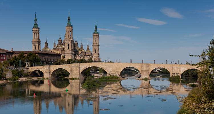 Pont de pierre historique avec tours de cathédrale et reflet de rivière.