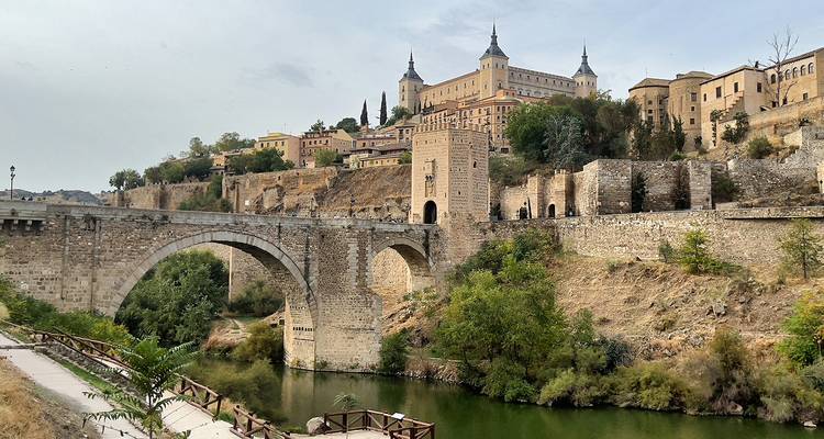 A stone bridge over a river with historic buildings on a hill.