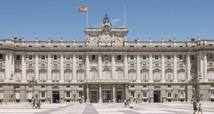 Façade avant du Palais Royal de Madrid avec le drapeau espagnol flottant au-dessus d'une plaza ensoleillée