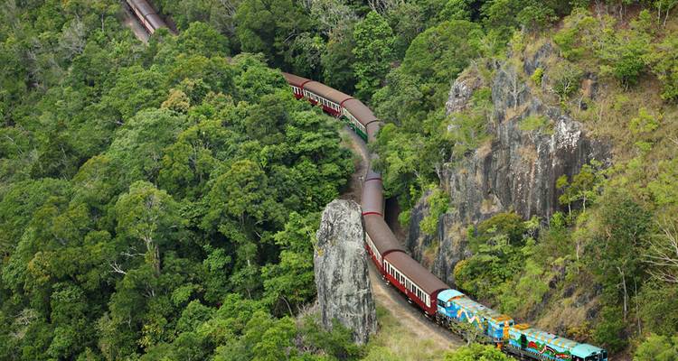 Trein slingerend door weelderig groen en rotsachtige kliffen.