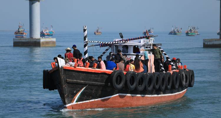 Boot voller Menschen auf einem Fluss mit entfernten Booten, Dwarka, Indien.