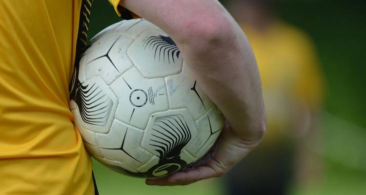 Persona sosteniendo un balón de fútbol americano contra su cadera.