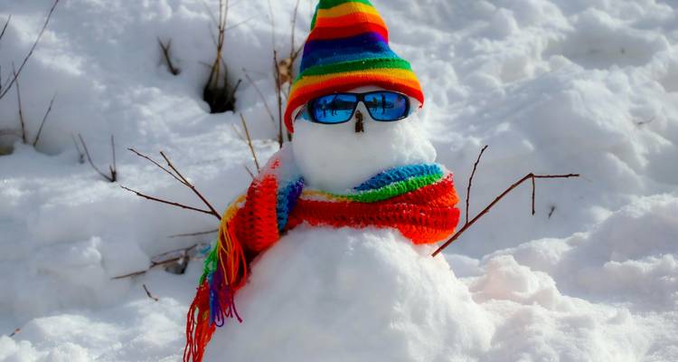 Un bonhomme de neige avec des lunettes de soleil et un chapeau et une écharpe colorés.