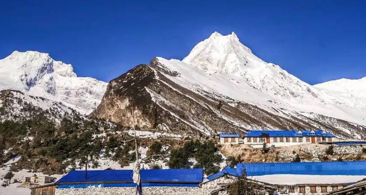 Un village avec des bâtiments aux toits bleus sur fond de montagne enneigée.