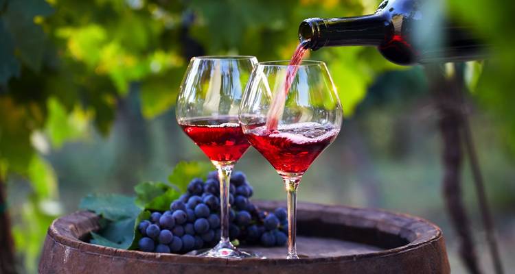 Wein wird in Gläser gegossen, mit Trauben auf einem Fass.