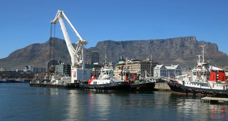 Puerto con barcos y grúas, respaldado por una gran montaña.