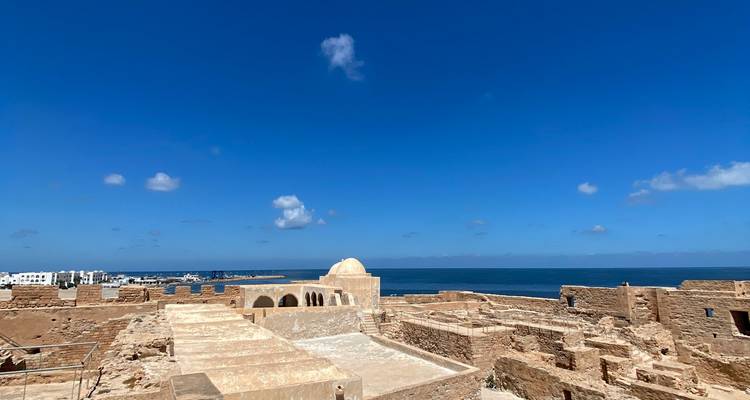 Paysage historique avec ruines au bord de la mer sous un ciel clair.