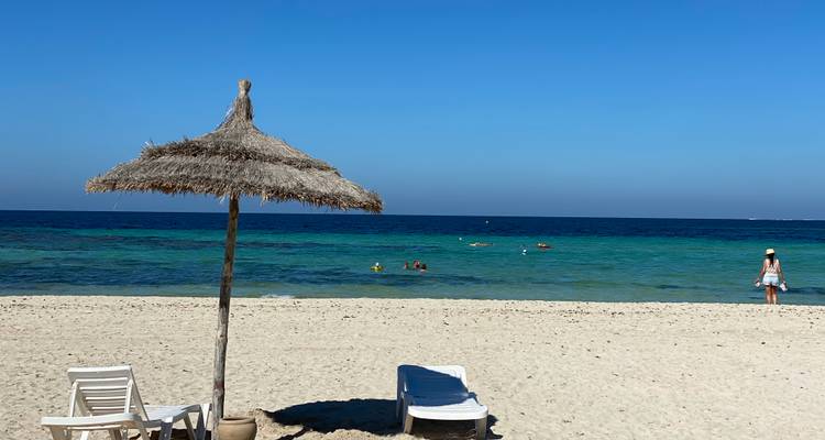 Scène de plage avec parasol, océan et baigneurs de soleil.