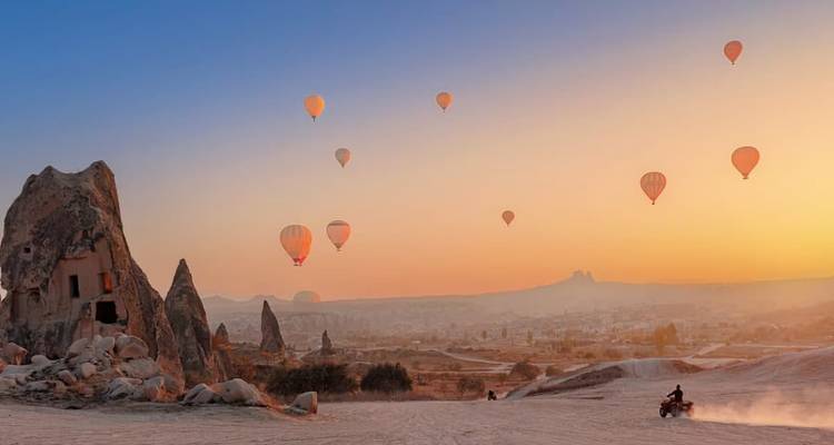 Plusieurs montgolfières flottant au-dessus d'un terrain rocheux au coucher du soleil.