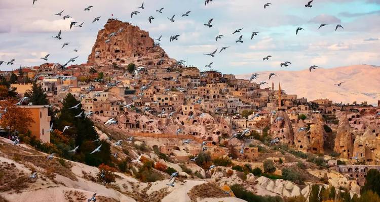Un village historique construit dans des collines rocheuses avec des oiseaux qui volent.