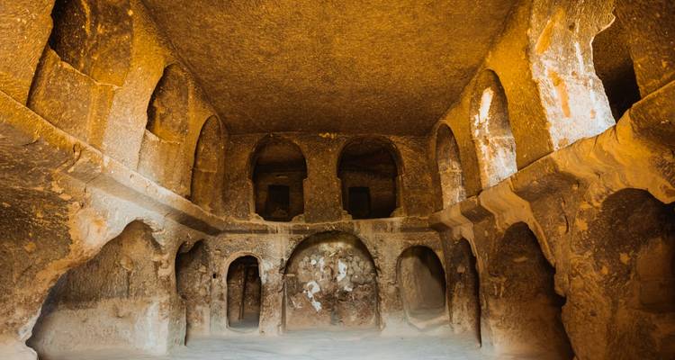 Un intérieur d'une chambre taillée dans la roche avec des arches et des piliers.