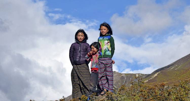 Drie kinderen in traditionele kleding op een heuveltop.