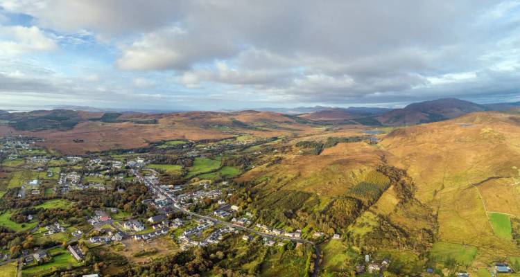 Luchtfoto van een klein plattelandsdorpje tussen lappendekensvelden, bossen en lage bergen.