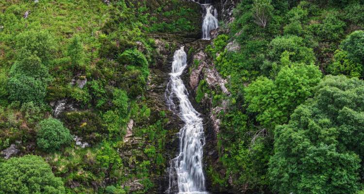 Meerlaags waterval stort zich door een mosachtig boskloof omgeven door dicht groen.