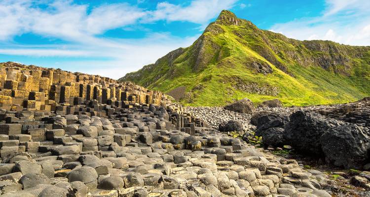 Close-up of the striking basalt columns of Giants Causeway with green hills.
