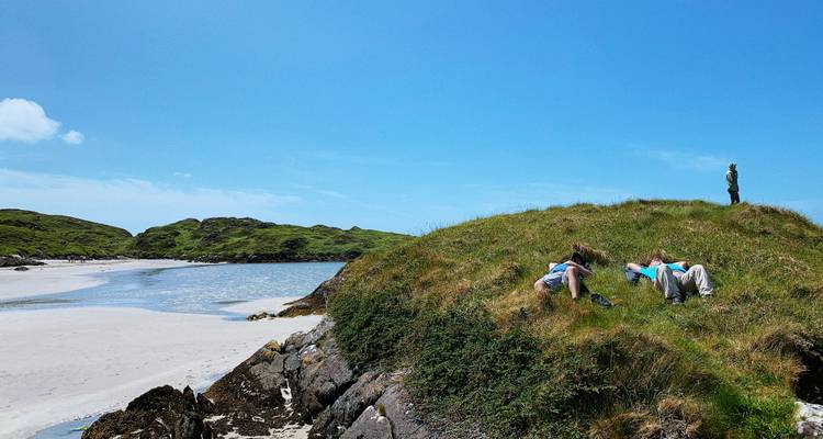 Menschen entspannen auf grasbewachsenen Dünen an einem Sandstrand.