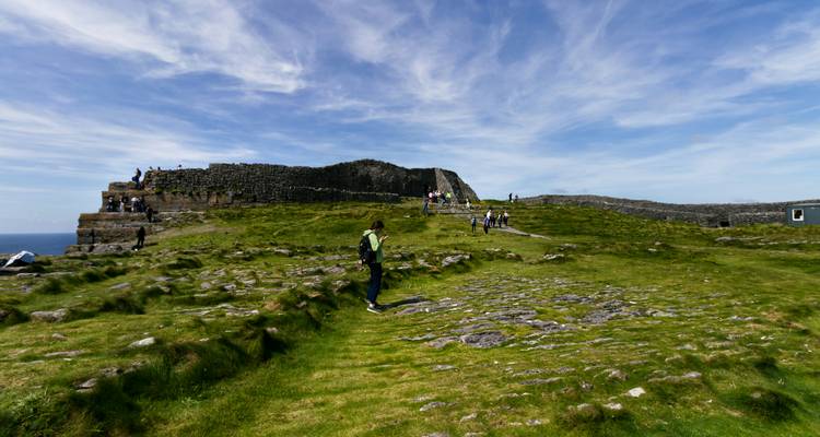 Visiteurs devant une structure de pierre historique dans un paysage herbeux.