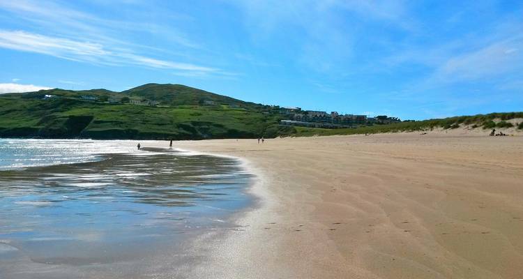 Une étendue de plage de sable avec une mer calme et des collines au loin.