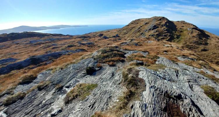 Crête rocheuse de chaumes dorés des landes surplombant l'Atlantique et des péninsules lointaines par beau temps.