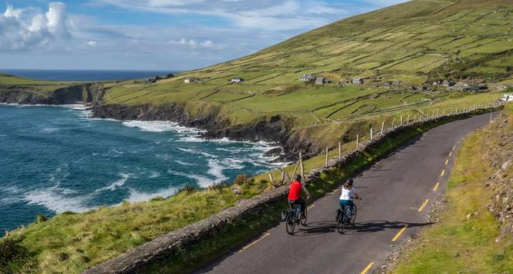 Zwei Radfahrer fahren entlang einer gewundenen Küstenstraße mit Blick auf dramatische Klippen und blaue Atlantikwellen.