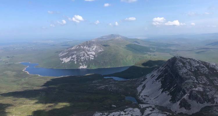 Luchtfoto van ruige bergtoppen en donkerblauwe meren onder een hemelsblauw met verspreide wolken.